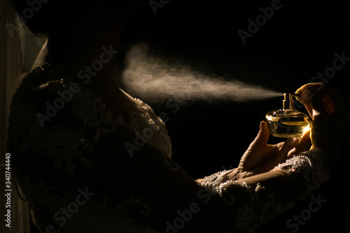 Mulher passando perfume no seu colo, com uma luz em meio a escuridão. Um frasco de perfume sendo segurado por uma pessoa photo