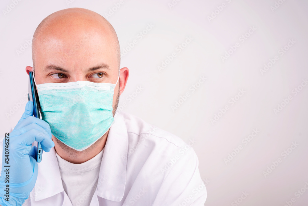 Man in face mask on white background with copy space talking by phone and makes a medical visit. Health care and protection while pandemic and covid-19. Business during quarantine and coronavirus. Man in face mask on white background with copy space talking by phone and makes a medical visit. Health care and protection while pandemic and covid-19. Business during quarantine and coronavirus.