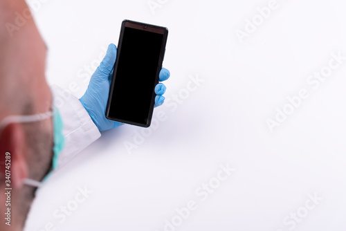 Man in face mask and protective gloves holding phone with blank screen with mock up on white background with copy space. Coronavirus and protection while covid-19. Pandemic and quarantine. 