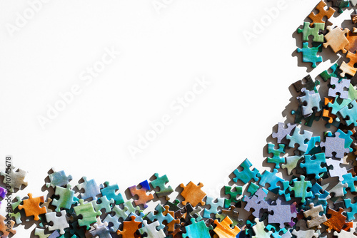 Top view of scattered multicolored jigsaw puzzle pieces. Lying on white table arranged as frame for copy space. Concept of putting together disconnect elements.
