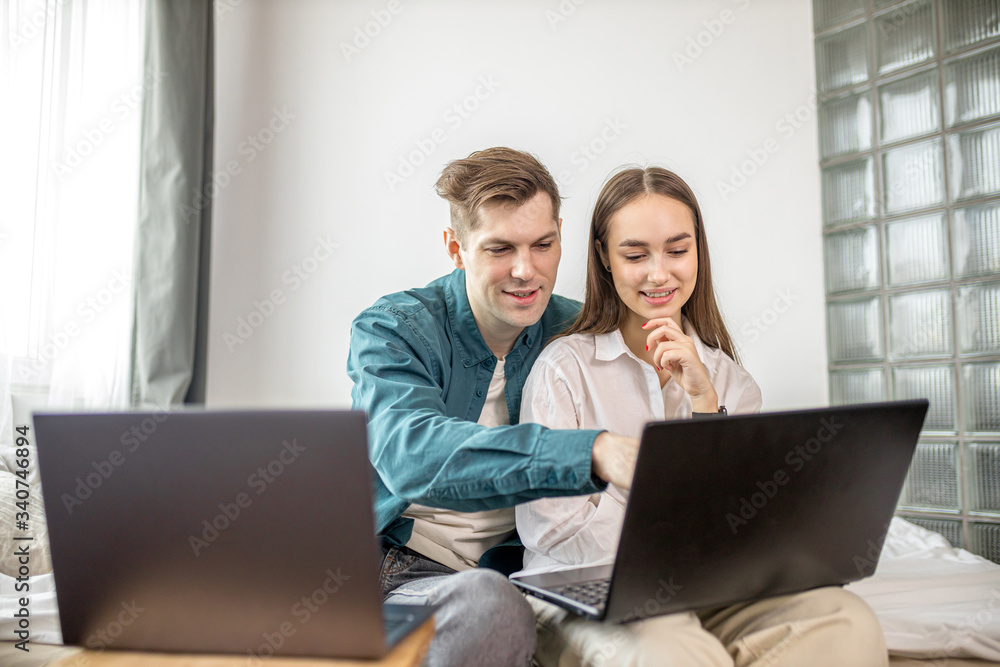 young married couple use their personal laptop. woman sit watching serials while her husband working from home, freelance. both look at screen of laptop and smile. indoors