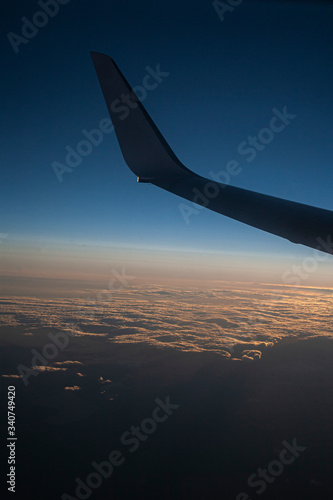 A VIEW OF THE PLANE'S WING AT SUNSET OVERLOOKING THE SKY AND CLOUDS