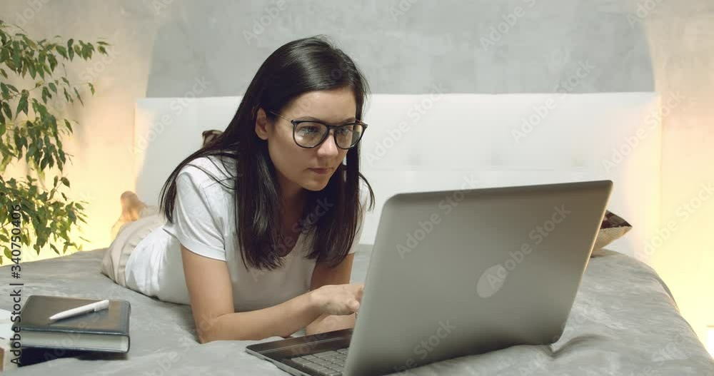 Young woman typing on a laptop keyboard. Female freelancer or student working writing post comments in social networks lying on the bed at home. Young woman typing on a laptop keyboard. Female freelancer or student working writing post comments in social networks lying on the bed at home.