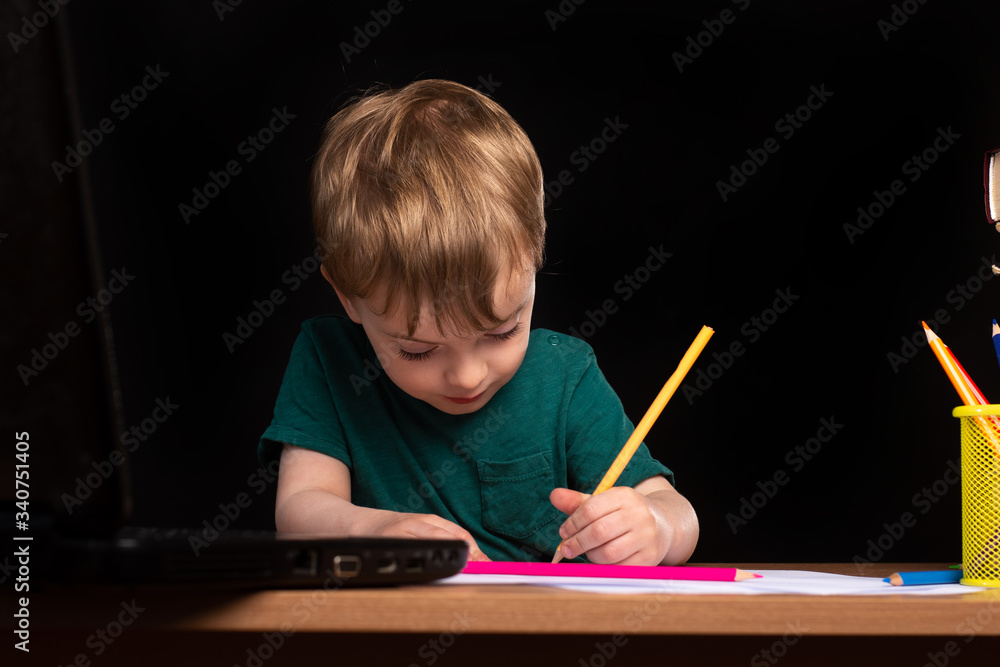 little boy does homework at a table with a laptop and books. the child writes. Black background. isolate. little boy does homework at a table with a laptop and books. the child writes. Black background. isolate.