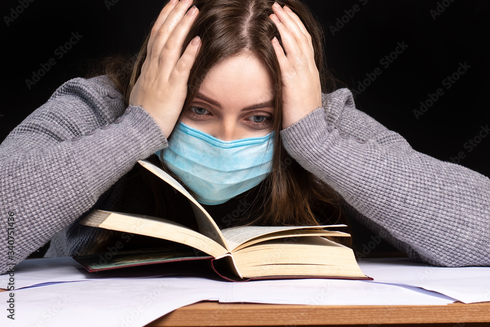 a young girl sitting above a book holding her hands behind her head. in a blue medical mask. quarantine. emotional portrait a young girl sitting above a book holding her hands behind her head. in a blue medical mask. quarantine. emotional portrait