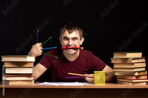 a young man holds pencils in his teeth and hand. emotions. office employee.