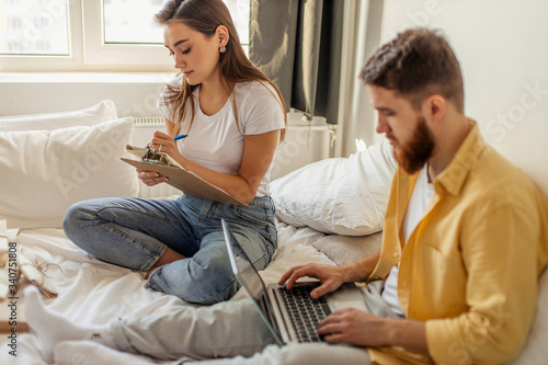 young caucasian married couple sort out letters invitations for housewarming. beautiful woman and handsome man sit with laptop at home, a lot of letters around