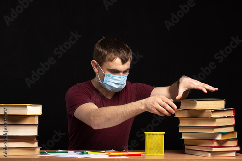 a young man in a medical mask selects a book from a pile. quarantined training. Black background.