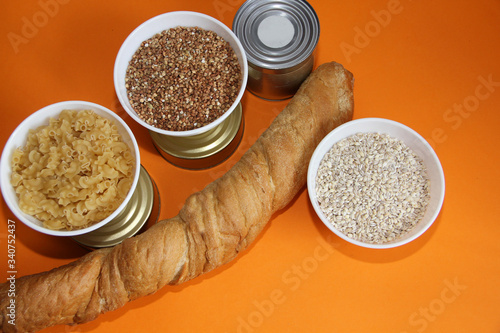 long-term storage food cereals, stew, sprats, bread and canned food on an orange background