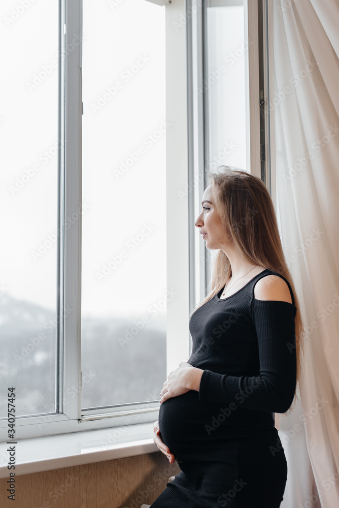 A pregnant girl is breathing fresh air from the window