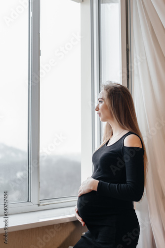 A pregnant girl is breathing fresh air from the window © Andrii
