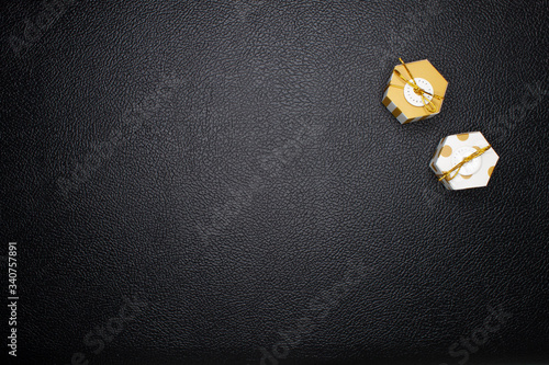 Flat layout of two golden gift boxes in a corner of black leather background