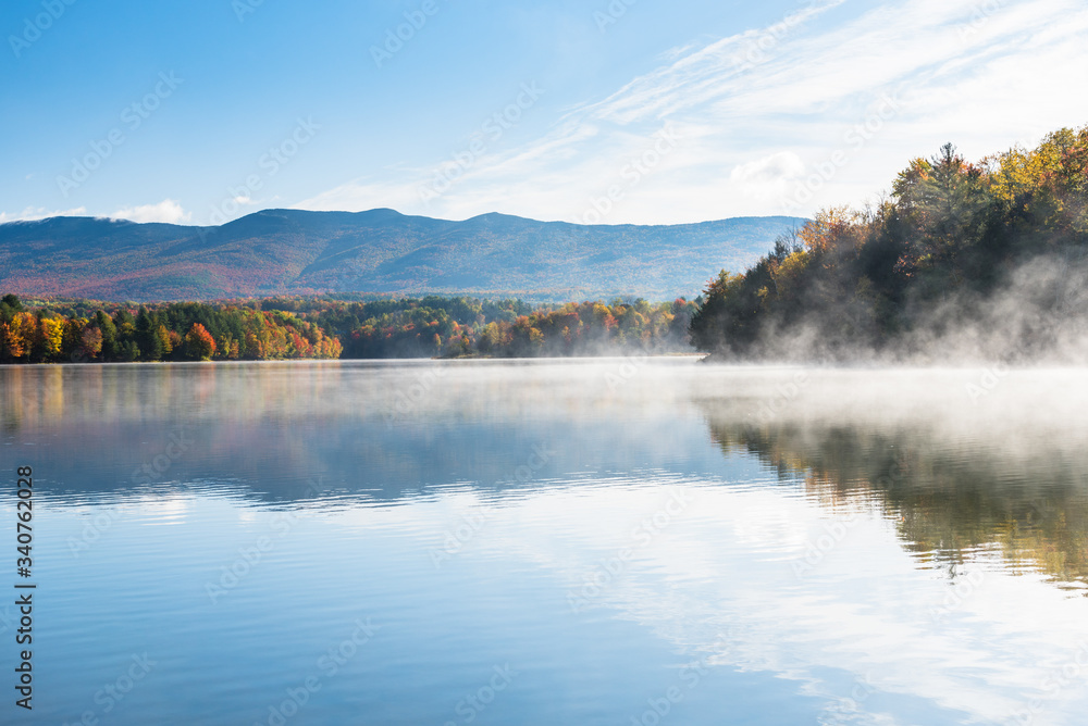 Majestic mountain lake partly covered in morning fog in autumn. Stunning autumn colours.