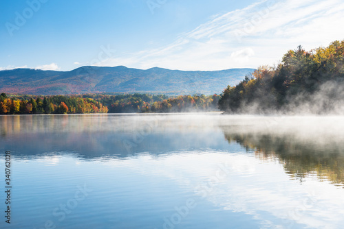 Majestic mountain lake partly covered in morning fog in autumn. Stunning autumn colours.