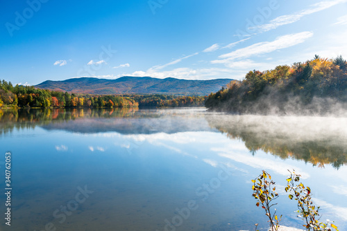 Beautiful lake in a wooded mountain landscape on a sunny autumn morning. A patch of lifting morning fog is visible on the right side of the picture.