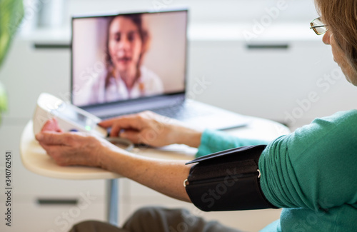 telemedicine concept elderly woman speaking to her doctor online and taking her blood pressure