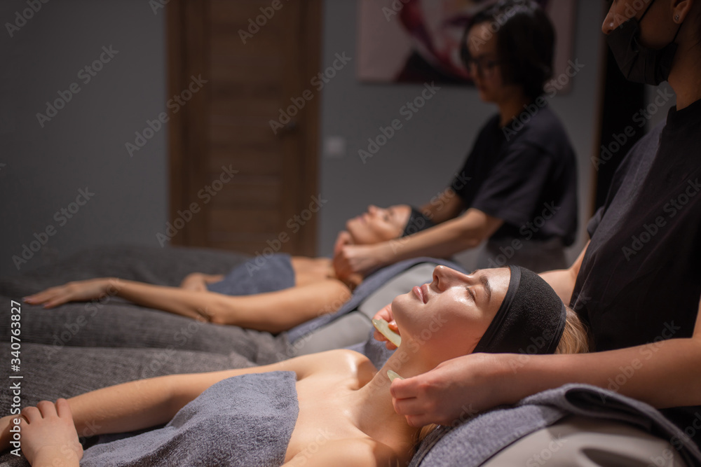 Obraz premium professional masseurs doctors doing anti-aging massage to female clients. beautiful women enjoys face and neck massage in spa salon