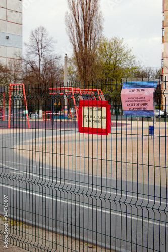 Kharkov, Ukraine, 18.04.2020:
Closed on 
quarantine by covid-19 kids playground with tied of white and red boundary tape in carantin time with warning 
sign, medium shot  photo