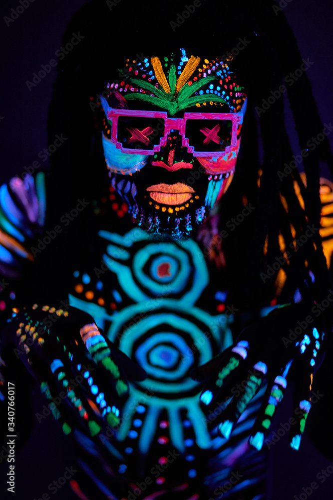 bright UV body art, fluorescent paint, young african dancer man in sunglasses, dark isolated studio background