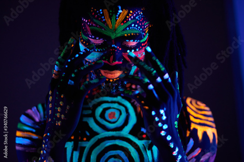 fantastic mysterious african male with UV body art posing at camera, futuristic body art, fluorescent paints glows in neon light
