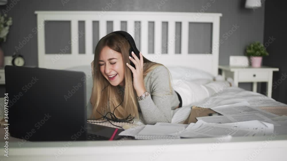 Young woman with headphones lying on the bed and matching a funny video Young woman with headphones lying on the bed and matching a funny video