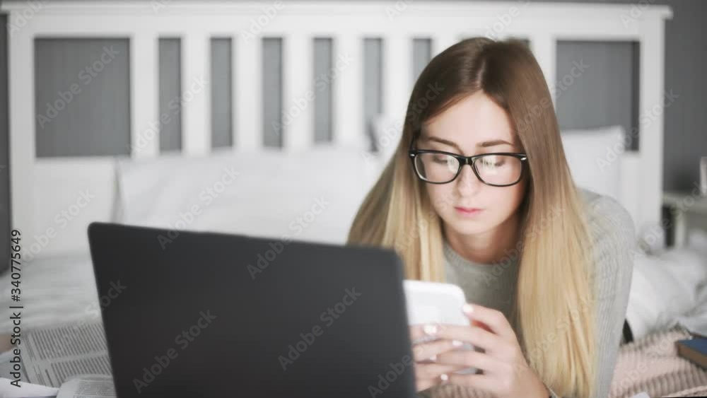 Young woman with galsess lying on the bed and using smartphone Young woman with galsess lying on the bed and using smartphone