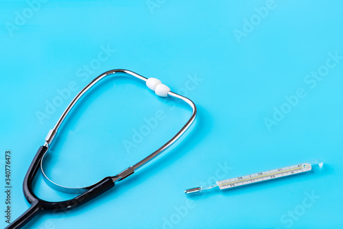 Stethoscope and glass thermometer for measuring body temperature on a blue background. Copy space. Empty space for inserting text