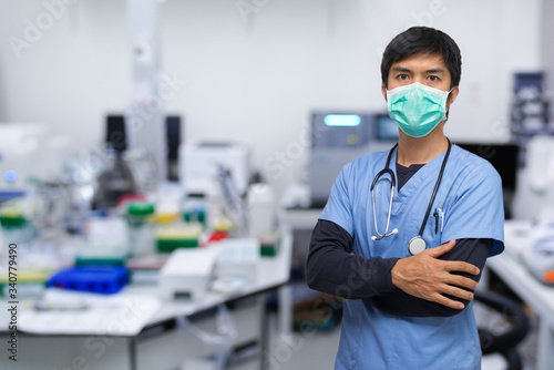 portrait of a Asian young man nurse/Doctor/scientist wearing surgical mask and standing with his arms crossed, Laboratory background