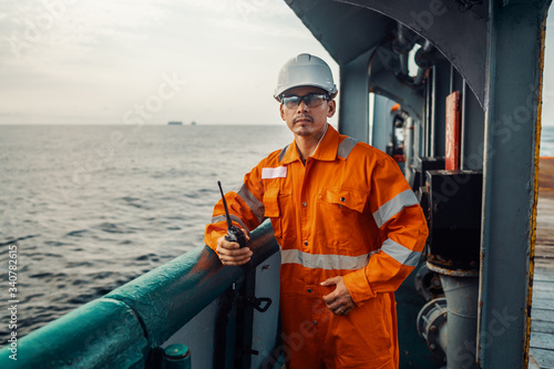 Filipino deck Officer on deck of vessel or ship , wearing PPE personal protective equipment. He holds VHF walkie-talkie radio in hands. Dream work at sea photo