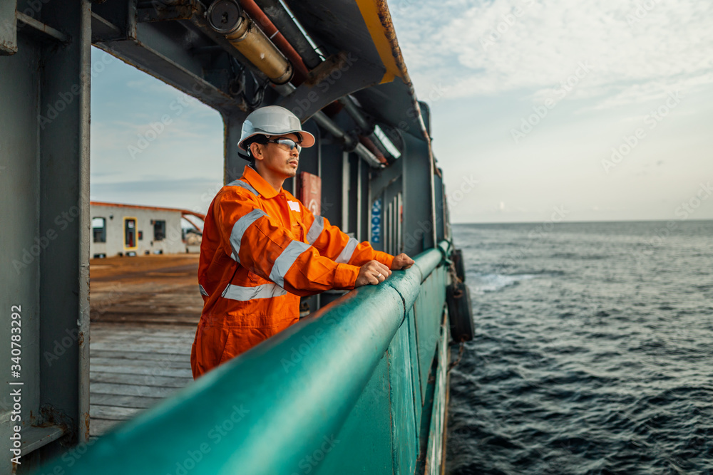 Filipino deck Officer on deck of vessel or ship , wearing PPE personal protective equipment - helmet, coverall, lifejacket, goggles. Safety at sea. He is tired