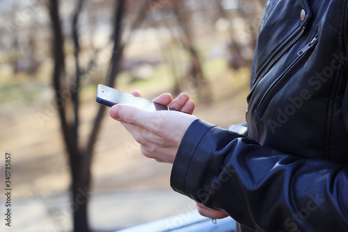 Man in a black leather jacket holds a smartphone in his hand close up.