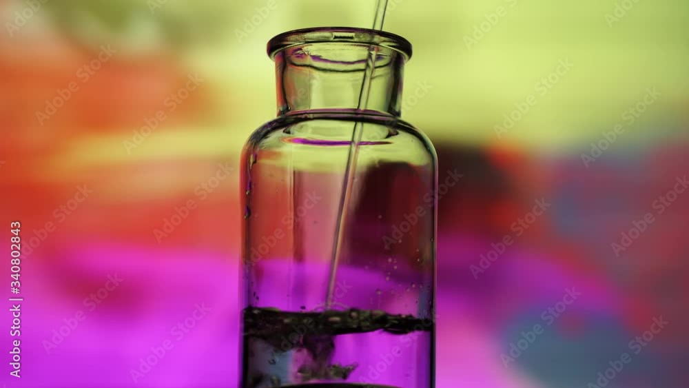 Stream of transparent liquid pouring into chemistry lab jar lit from behind with neon lights. Stream of transparent liquid pouring into chemistry lab jar lit from behind with neon lights.