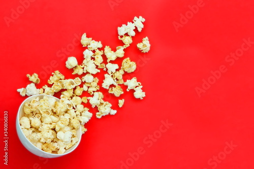 Top view isolated salted popcorn mix with cheese popcorn spilled from white bowl on red table background, movie cinema time concept, have copyspace