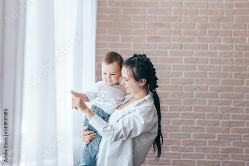 Happy mother with small sun standing near window at home, leisure with children © Anastassiya 