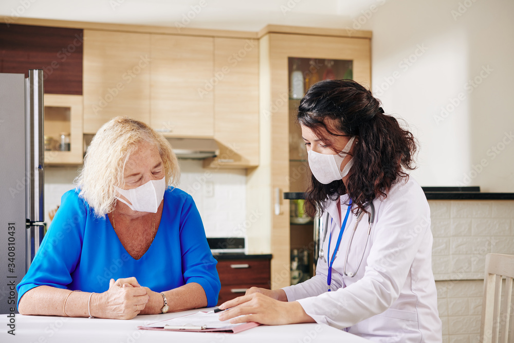 Young female doctor in medical mask showing prescription to senior patient Young female doctor in medical mask showing prescription to senior patient