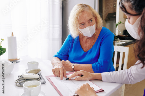 Doctor in medical mask visiting senior patient at home and explaining her results of cardiogram