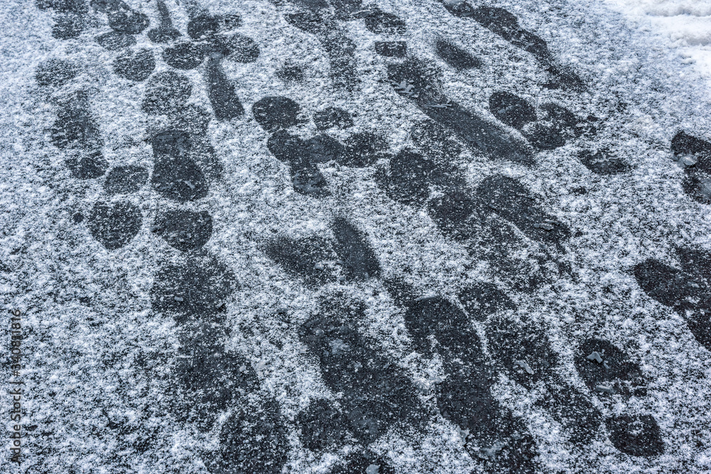 many footprints on shoes on asphalt pavement covered with snow