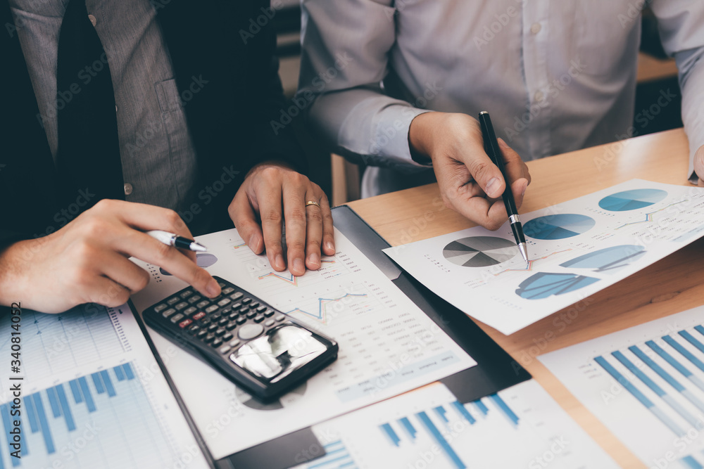 Manager calculates about the company finances by pressing on the calculator on the table with the employee explaining the summary report of the company cost at the office. Manager calculates about the company finances by pressing on the calculator on the table with the employee explaining the summary report of the company cost at the office.