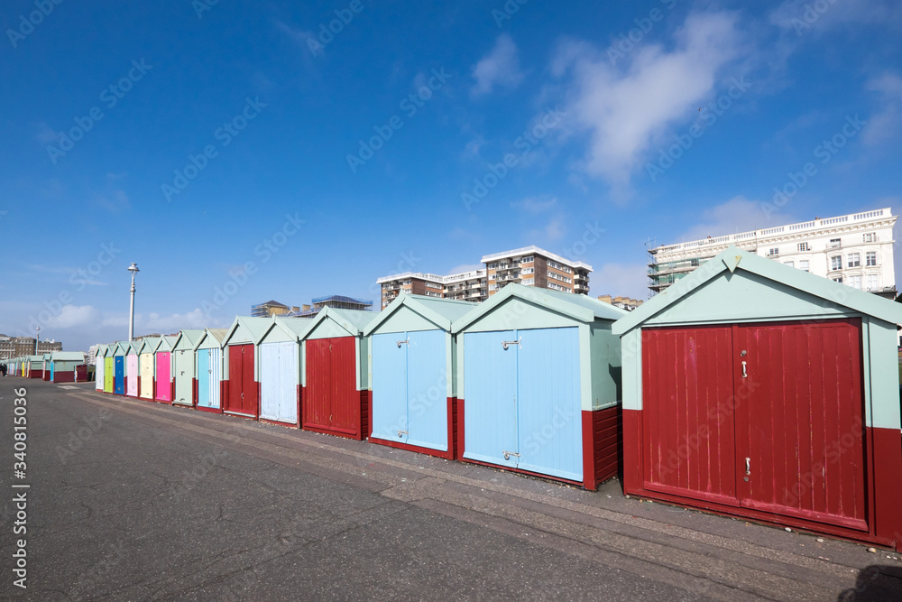 Beach huts on Hove seafront in Brighton, Sussex, UK, with apartment block buildings with blue sky Beach huts on Hove seafront in Brighton, Sussex, UK, with apartment block buildings with blue sky