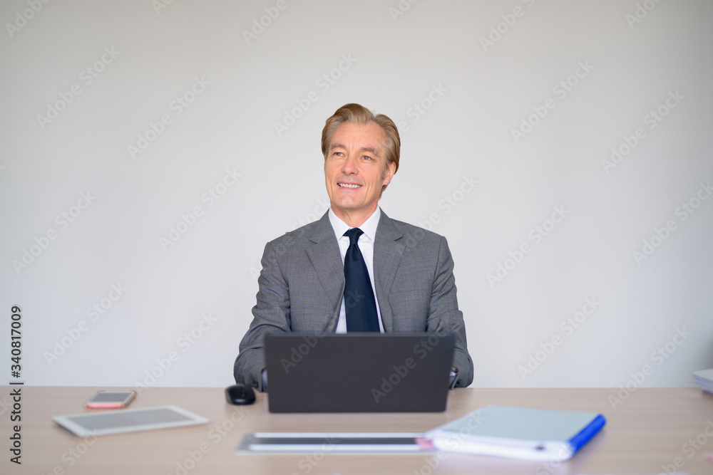 Happy mature handsome businessman thinking while using laptop at work Happy mature handsome businessman thinking while using laptop at work