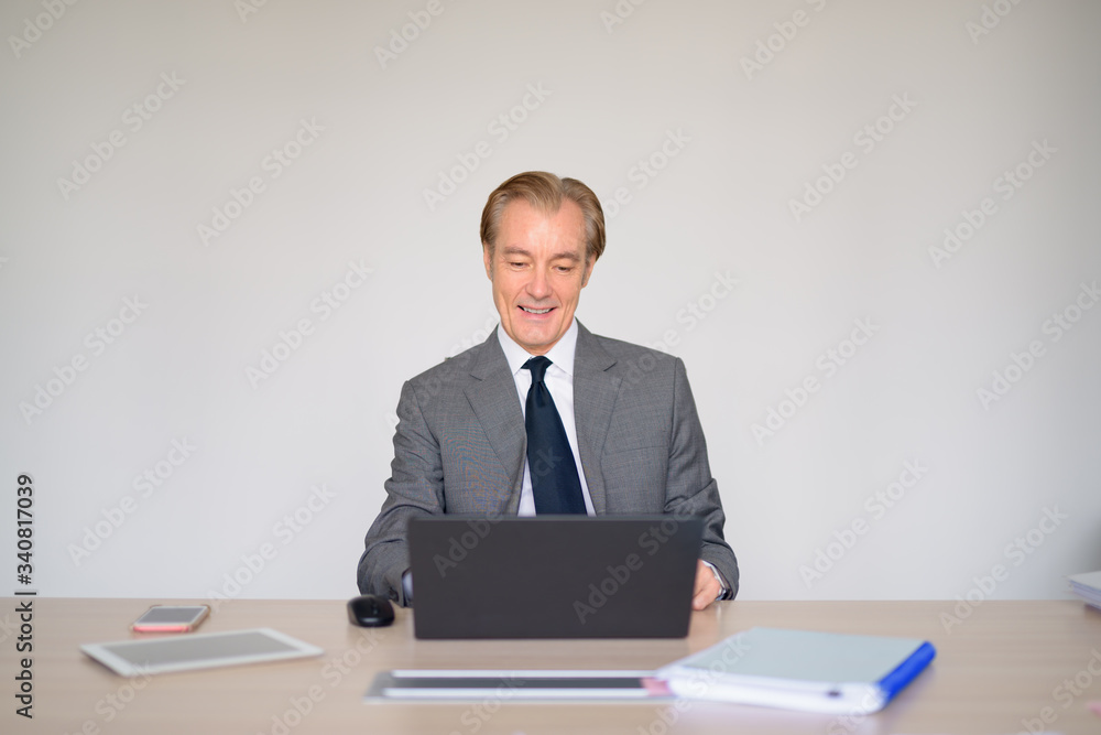 Happy mature handsome businessman in suit using laptop at work Happy mature handsome businessman in suit using laptop at work