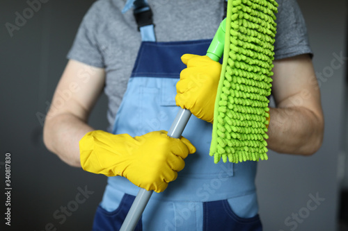 Man in work clothes, cleaning agent, holds mop. Wet cleaning in house or apartment using household cleaning products. House cleaning during pandemic. Decontamination and destruction viruses