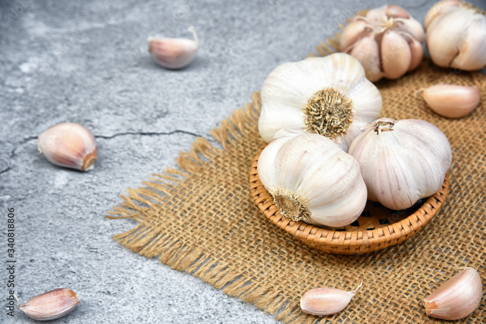 Organic Garlic. Fresh Garlic Cloves and Garlic bulb in wooden basket on dark background with Pile of garlic or spice. Selected focus. Concept of spices for healthy cooking. Organic Garlic. Fresh Garlic Cloves and Garlic bulb in wooden basket on dark background with Pile of garlic or spice. Selected focus. Concept of spices for healthy cooking.