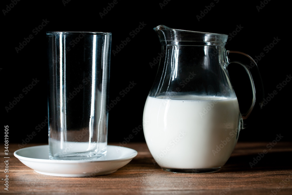 Una taza de cristal vacía y una jarra de leche de vaca en una mesa de madera Una taza de cristal vacía y una jarra de leche de vaca en una mesa de madera