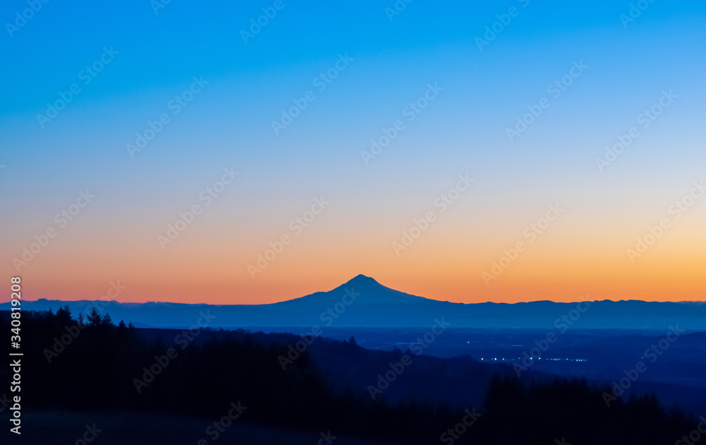 A sunrise scene in Oregon, with the iconic peak of Mt. Hood on the horizon in silhouette, vivid color behind.
