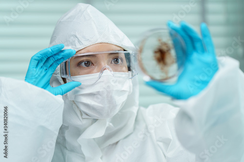 Coronavirus testing process  Woman hand in blue rubber gloves holding a virus sample in Petri dish in laboratory.