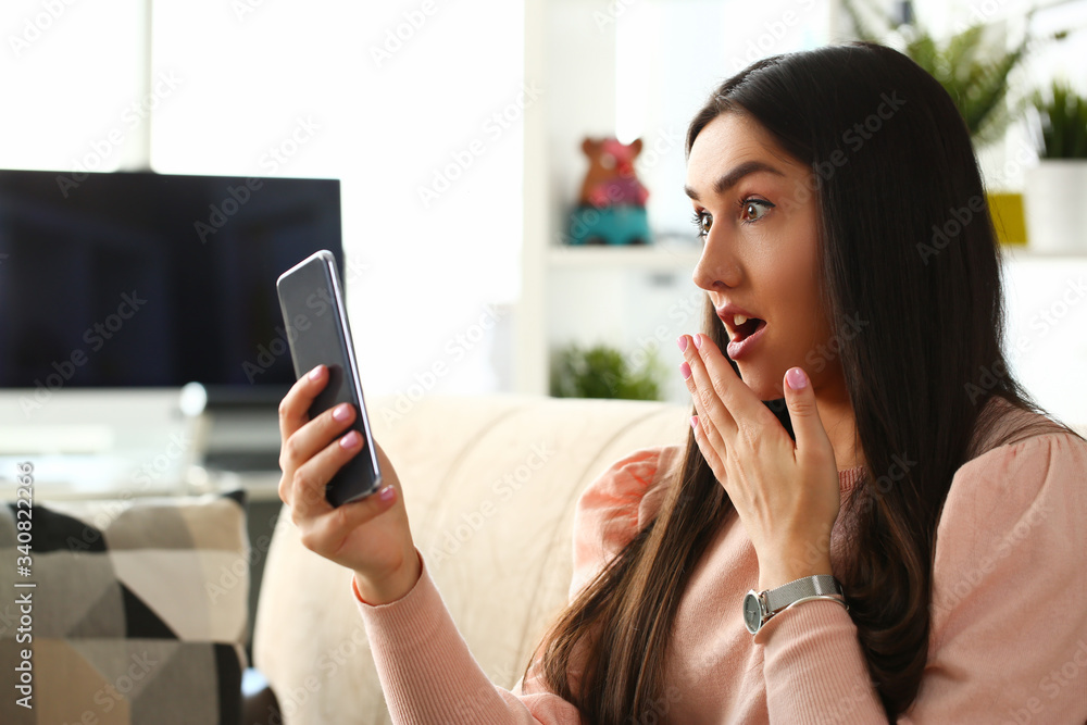Beautiful woman portrait sit at sofa look in smartphone and open mouth home background concept Beautiful woman portrait sit at sofa look in smartphone and open mouth home background concept