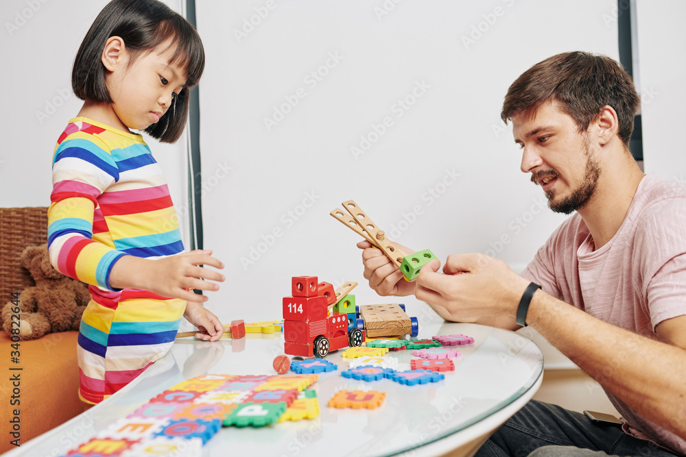 Young father helping daughter to make machine from wooden parts when they are playing at home Young father helping daughter to make machine from wooden parts when they are playing at home