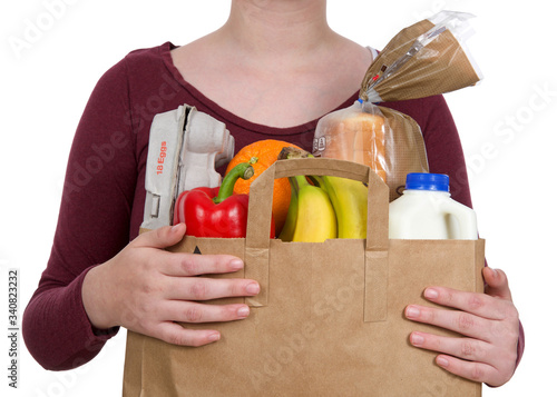 Young female holding brown eco friendly grocery bag with bottle of milk, carton of eggs, bag of bread, bananas, bell pepper and orange, isolated on white. Healthy shopping. photo