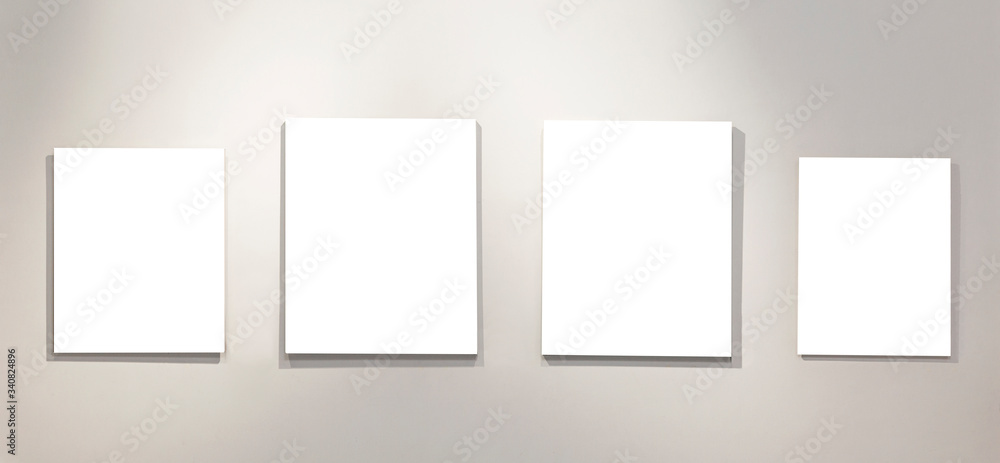 Four empty isolated on white paintings on the wall with gallery lighting. Space for text. Four empty isolated on white paintings on the wall with gallery lighting. Space for text.